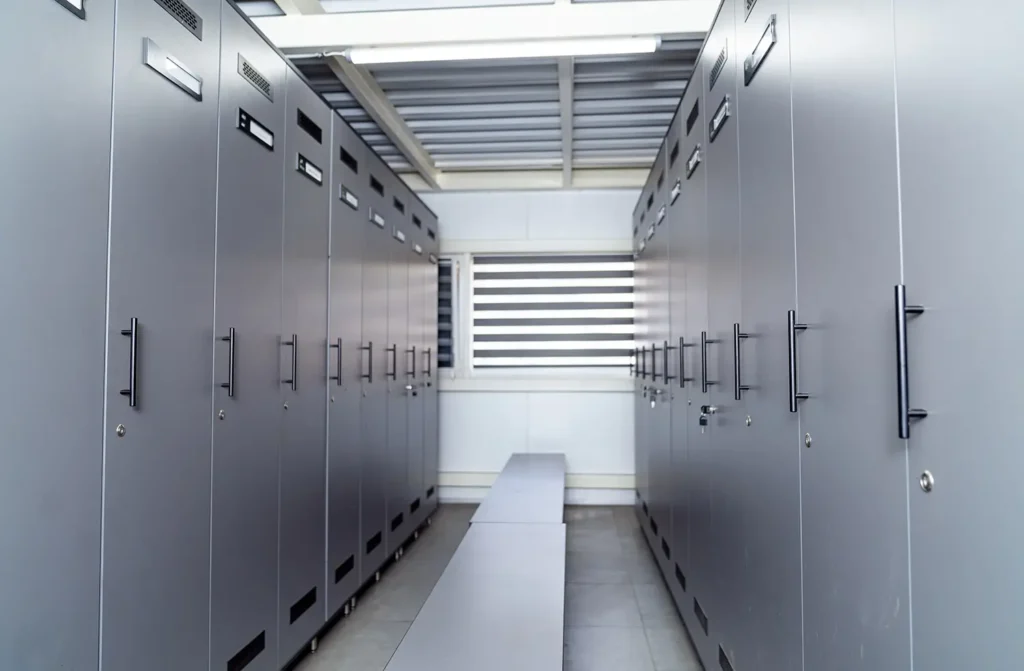 Ein leerer Umkleideraum mit grauen Spinden und einer Bank in der Mitte.